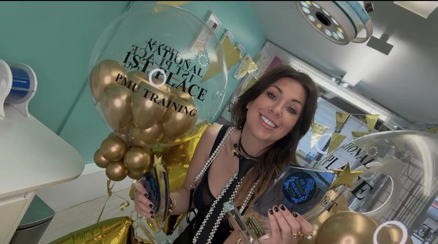 Katy Jobbins smiling and holding a trophy beside a clear balloon reading National 1st Place PMU Training, filled with gold balloons