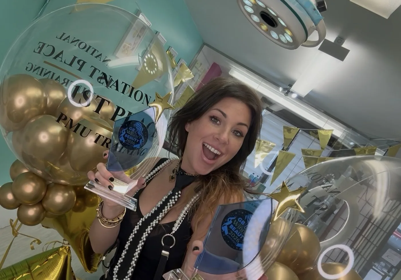 Katy Jobbins holding her two GB Beauty Awards 2026 trophies among National 1st Place balloons